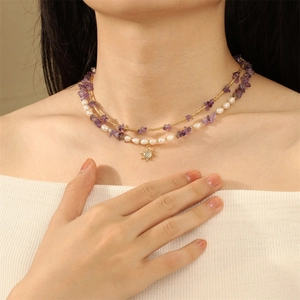 Detail of layered necklace featuring purple gravel stones, pearls, and a gold sun pendant