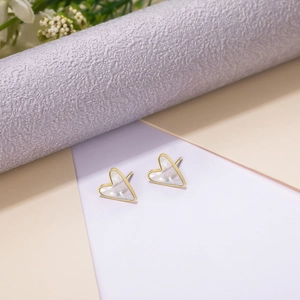 Close-up of heart-shaped gold studs with iridescent pearl inlay on a soft background