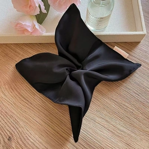 Detail of a black satin scarf scrunchie with a pink brand tag on a wooden surface