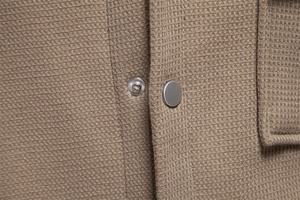 Detailed macro view of waffle knit fabric and matte silver metal snap button on brown jacket
