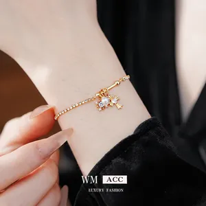 Bracelet doré scintillant avec croix, perle et strass porté au poignet