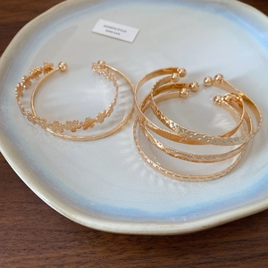 Detailed view of assorted gold open bangles with floral and star motifs on a ceramic plate