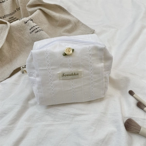 Detail of cream white quilted makeup bag with 3D floral accent and delicate lace embroidery