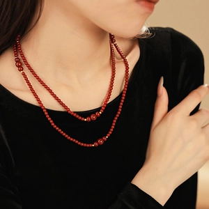Dettaglio di collana a doppio filo di perle rosso scuro con inserti dorati su velluto