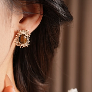 Close-up of vintage golden tiger eye stud earrings worn by a model in soft lighting