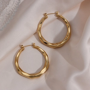 Large golden twisted hoop earrings for women on elegant beige silk background texture