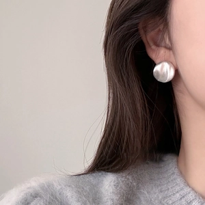 Detail of round silver earrings with matte brushed texture worn by a female model