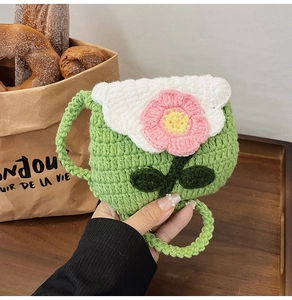 Close-up of green hand-knitted crochet bag with pink flower detail and white wave edge