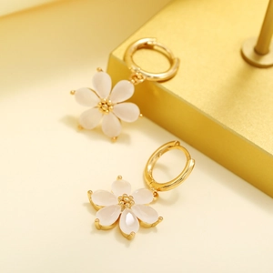 Macro shot of gold-plated hoop earrings with white cat-eye stone flower pendants
