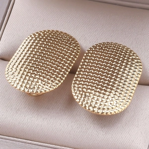 Macro shot of gold stainless steel earrings with intricate fish-scale textured pattern