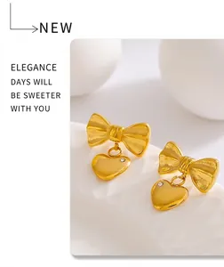 Detail of gold bow earrings with heart pendants and micro-inlaid stones on white background
