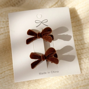 Close-up of two small coffee brown velvet bow hair clips on white card and knit fabric