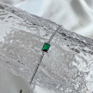 Detail of S925 silver tennis bracelet with emerald cut green stone on silk background