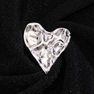 Vue macro d'une broche coeur argentée à texture de lave sur tissu plissé noir