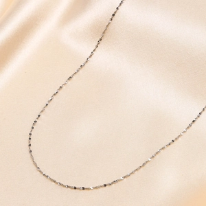 Macro shot of 1mm silver stainless steel snake chain on soft beige silk background