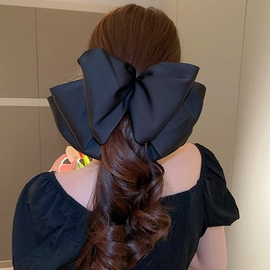 Détail d'une grande pince à cheveux avec nœud en satin noir porté par un modèle