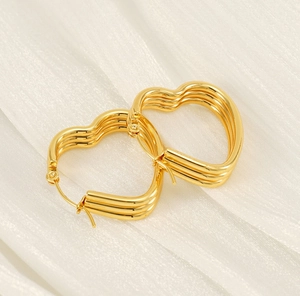 Détail de boucles d'oreilles cœur multicouches en or poli sur tissu de soie blanc