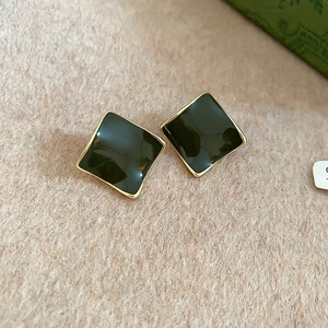 Close-up of 14k gold plated square earrings with dark green enamel on textured background