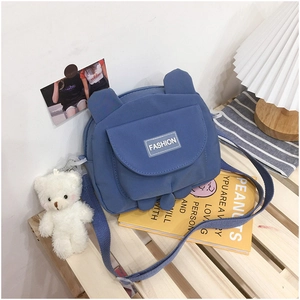 Blue cute bear canvas crossbody bag with fluffy charm on a cozy lifestyle desk setup