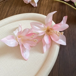 Detail of two silk fabric gradient pink hibiscus hair clips on a textured tray