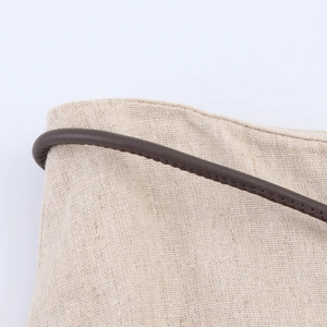 Dettaglio della trama in lino beige e del cinturino in pelle marrone scuro con cuciture