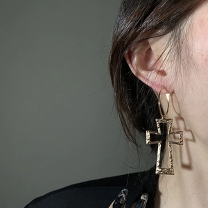Close-up of a vintage golden hollow cross earring with textured surface on ear