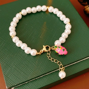 Detail of pearl bracelet with pink strawberry enamel pendant on a green jewelry box