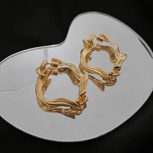 Modern twisted geometric gold hoop earrings with fluid metal texture on heart mirror