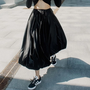Close-up of a flowing black satin midi skirt with high-shine finish on outdoor pavement