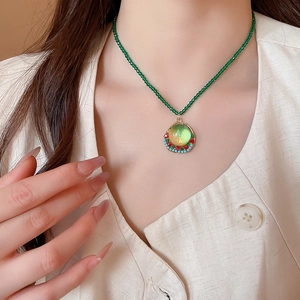 Detail of beaded necklace with green resin pendant and gold frame worn on a model