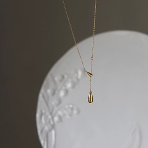 Minimalist gold double teardrop pendant necklace on elegant white porcelain background