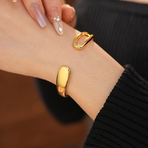 Detailed close-up of polished gold-plated open cuff bracelet on a model's wrist