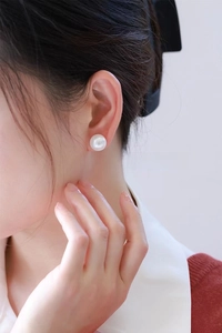 Close-up of 12-13mm faux pearl stud earrings worn on ear with lustrous white finish