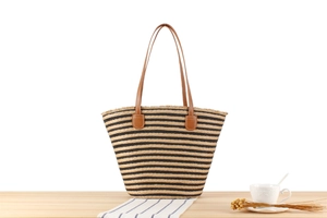 Close-up of woven tote bag featuring black stripes and brown leather handles on a desk