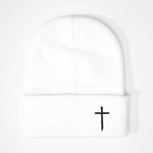 Close-up of white knitted beanie featuring detailed black cross embroidery on the cuff