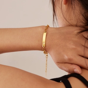 Detailed view of a gold chain bracelet featuring a polished nameplate with a zircon stone