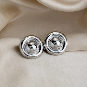 Vue macro de boucles d'oreilles minimalistes en argent poli sur tissu en soie champagne