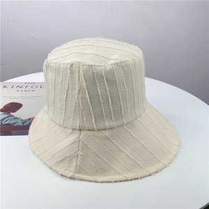 Détail d'un chapeau bob beige à rayures avec franges sur un support minimaliste
