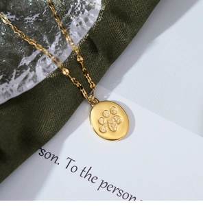 Detail shot of a golden oval pendant featuring an embossed cat paw on green satin