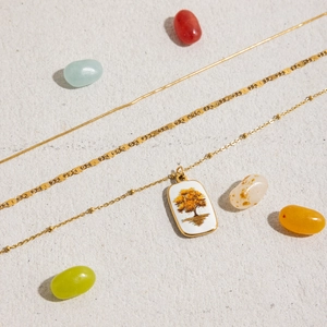 Détail du collier triple rangs en acier doré 18K avec pendentif arbre de vie et émail blanc