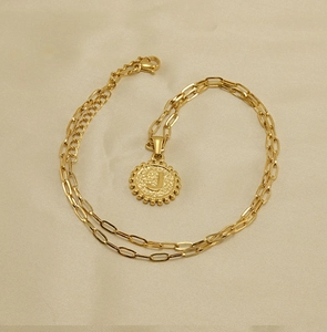 Detailed macro view of golden letter J pendant on paperclip chain over beige silk fabric