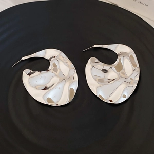 Macro shot of large abstract irregular geometric silver earrings with hammered texture finish