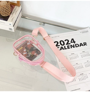 Detail view of pink transparent PVC crossbody bag with wide strap on glass desktop