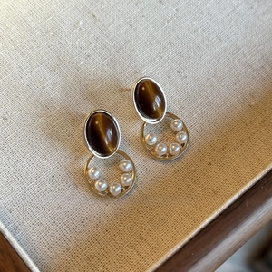 Macro view of geometric resin earrings with brown cat-eye stones and white pearls