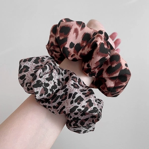 Set of two stylish leopard print fabric scrunchies worn on wrist with grey background
