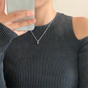 Close-up of a minimalist silver star cross pendant necklace worn on a ribbed sweater