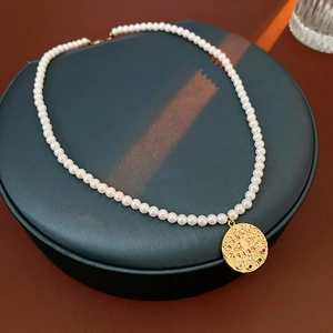 Gros plan du pendentif œil maléfique doré avec zircons sur un collier de perles lustrées