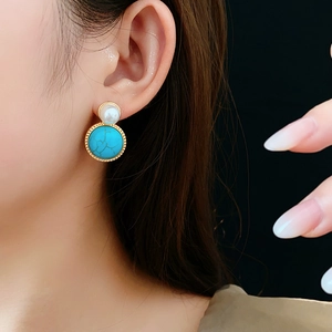 Close-up of vintage gold earrings with round white pearl and marbled green turquoise stone