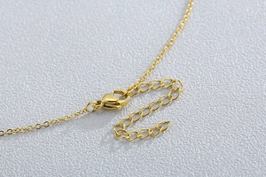 Détail du collier doré montrant le fermoir mousqueton et la chaîne d'extension sur fond gris