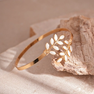 Close-up of gold olive leaf open bangle with white enamel on a natural beige stone